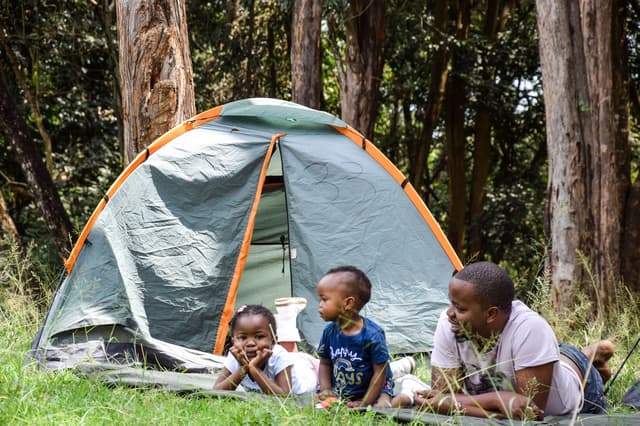 Family relaxing beside a camping tent in woodland