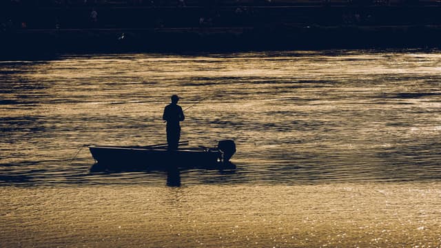 Person standing in a small boat on the lake at sunset