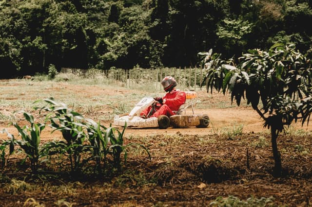 Driver in a red suit steering a dirt go-kart along the track